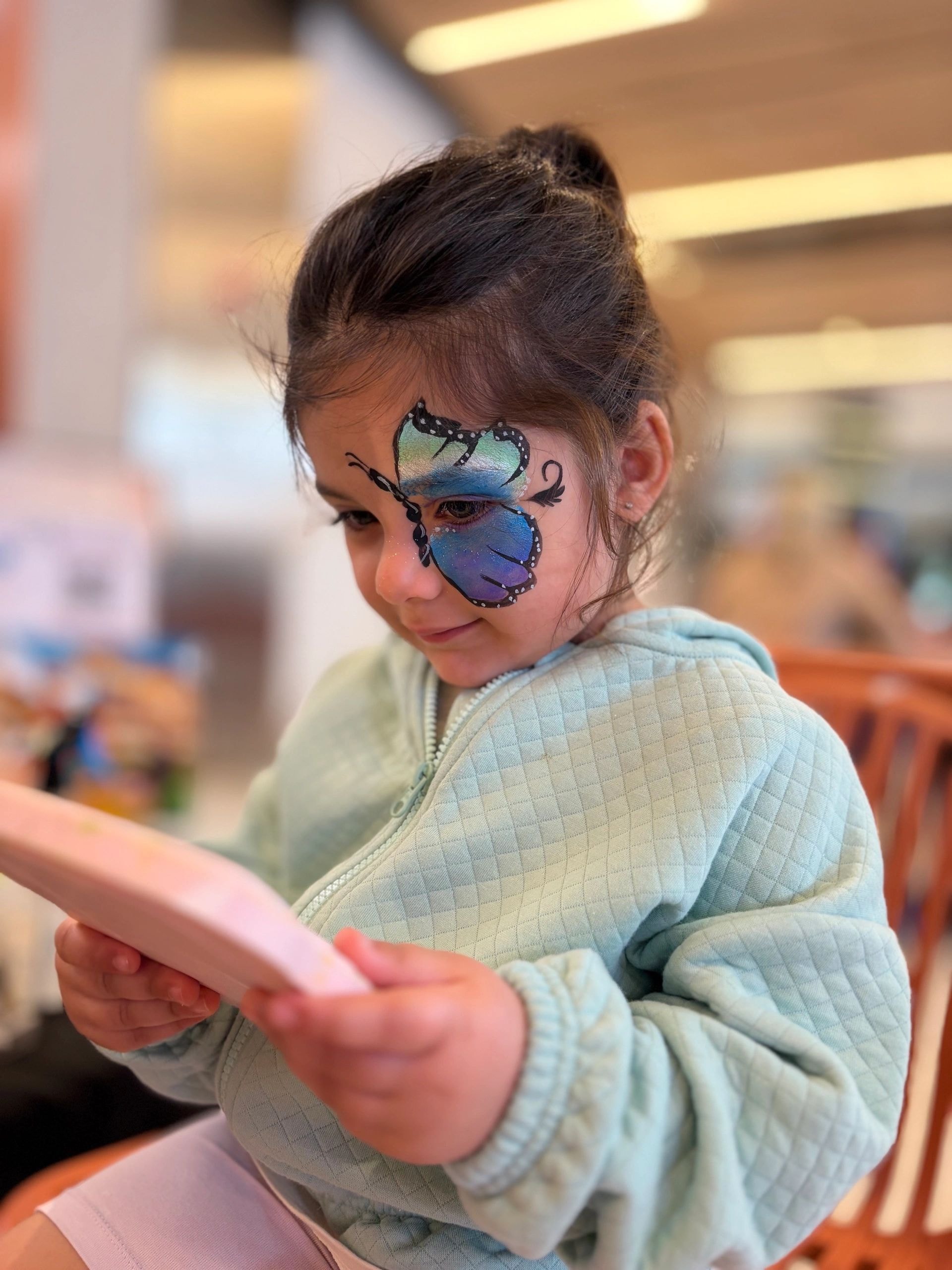 Child with butterfly face paint in blue jacket