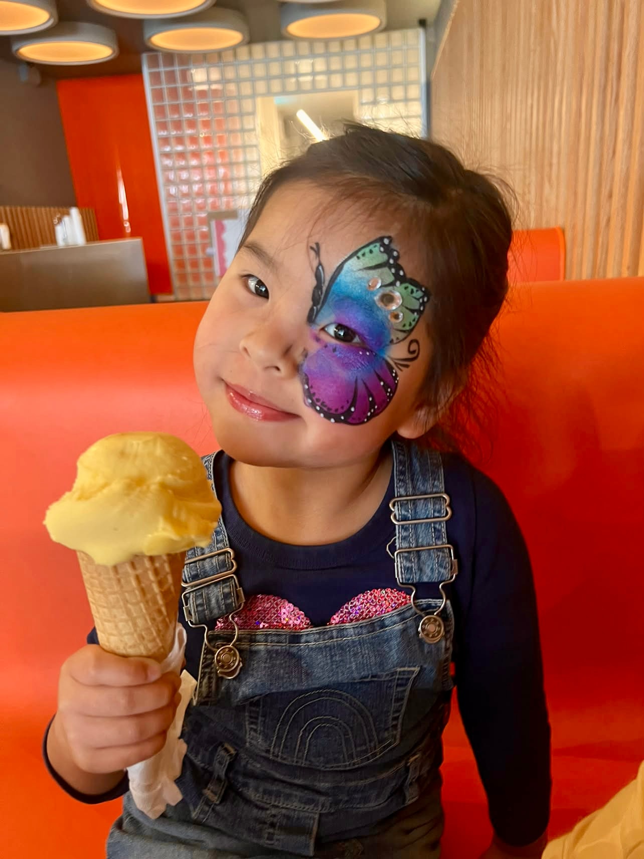 Child with butterfly face paint holding an ice cream cone