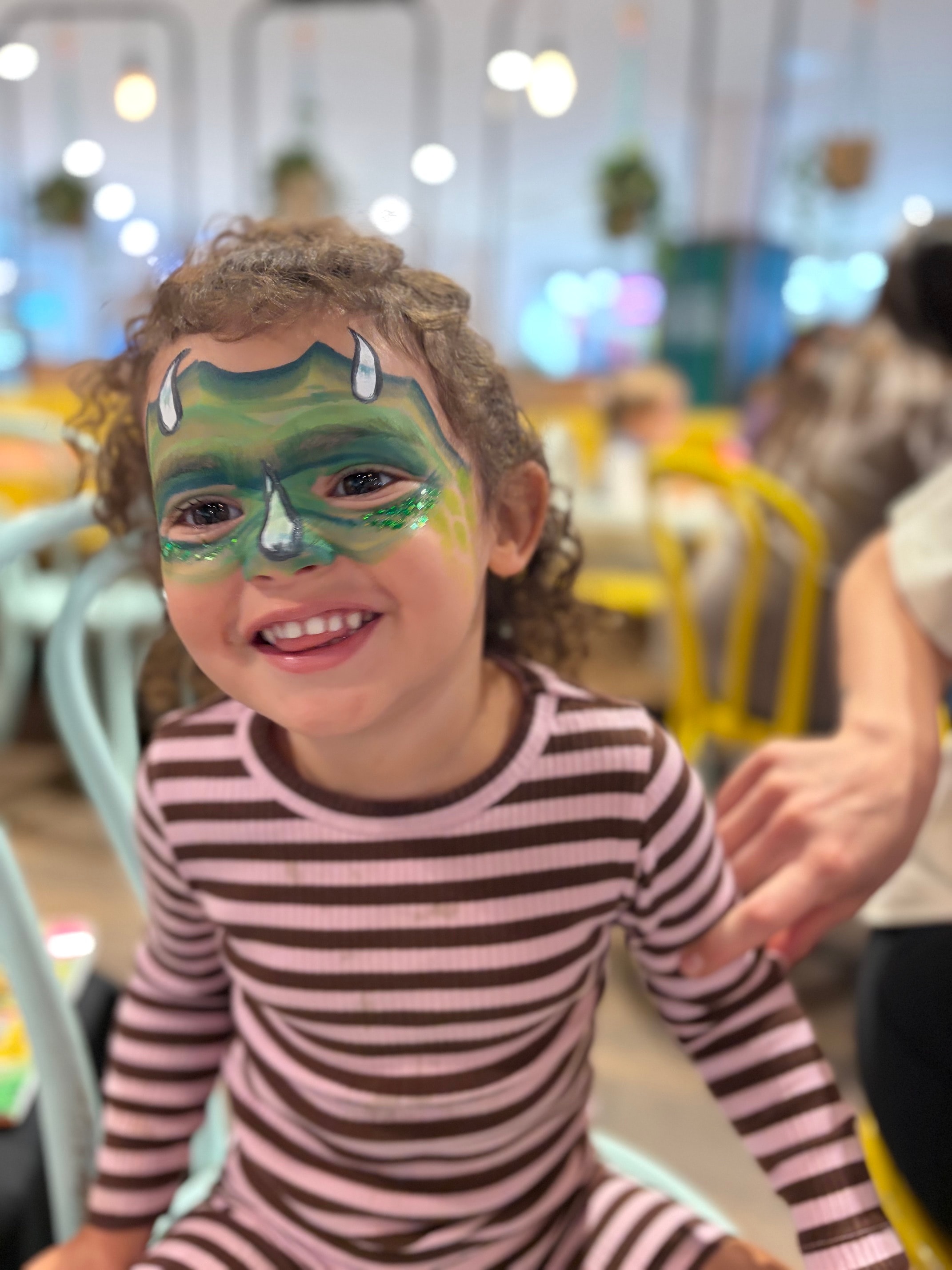 Toddler with green dinosaur face paint with white horns smiling