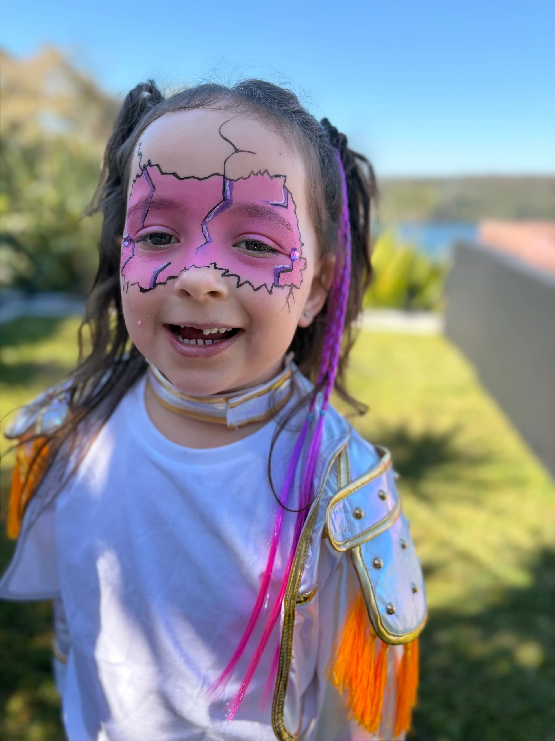 Child with pink and purple mask face paint outdoors