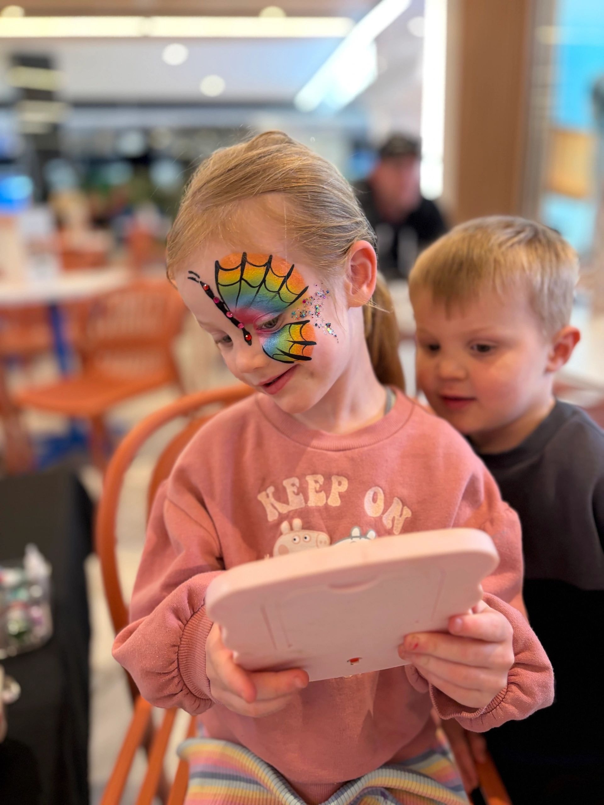 Child with rainbow butterfly face paint in pink shirt